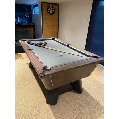 Pool table with cues and balls in a room with a dartboard on the wall.