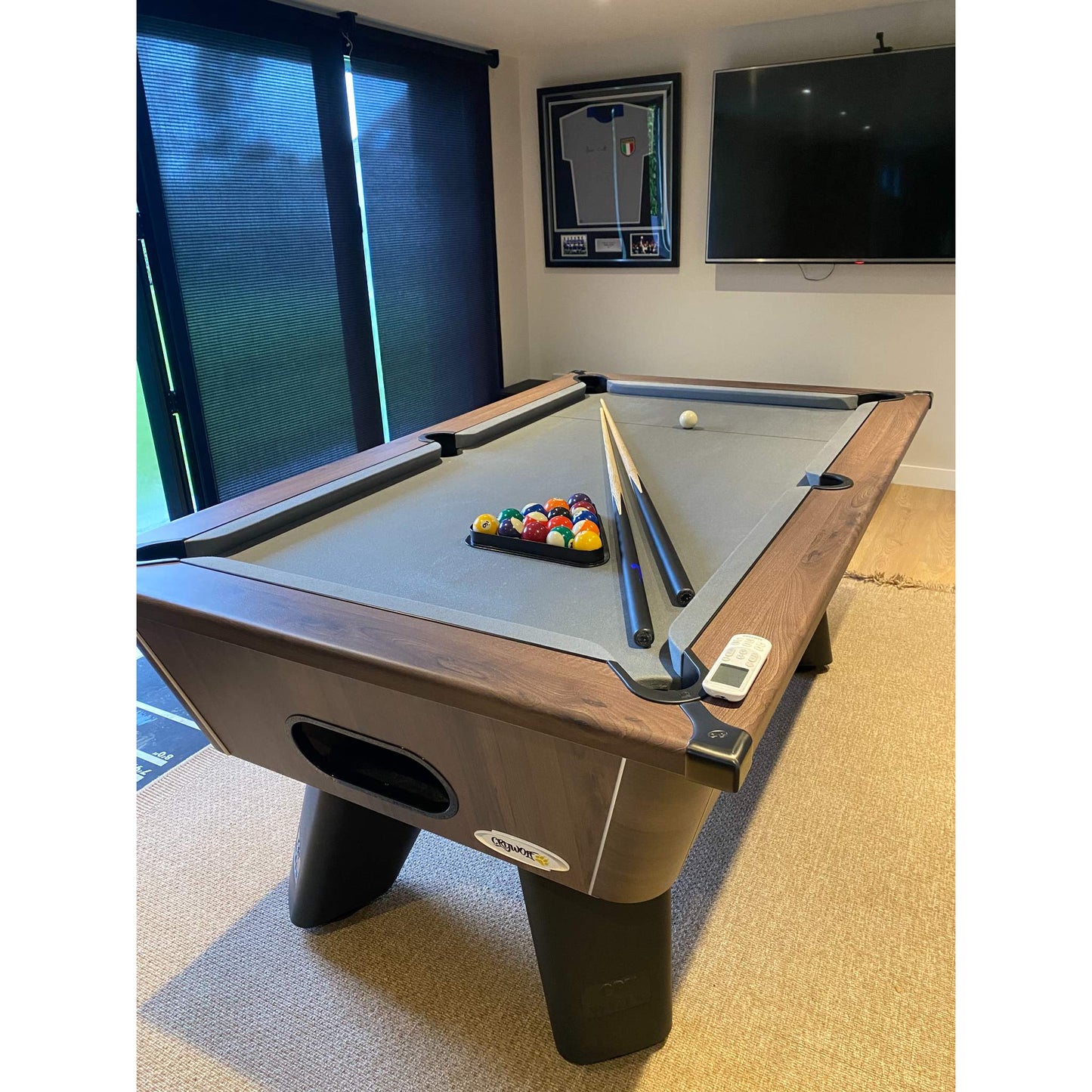 Pool table with balls and cues in a room with a television and framed picture on the wall.