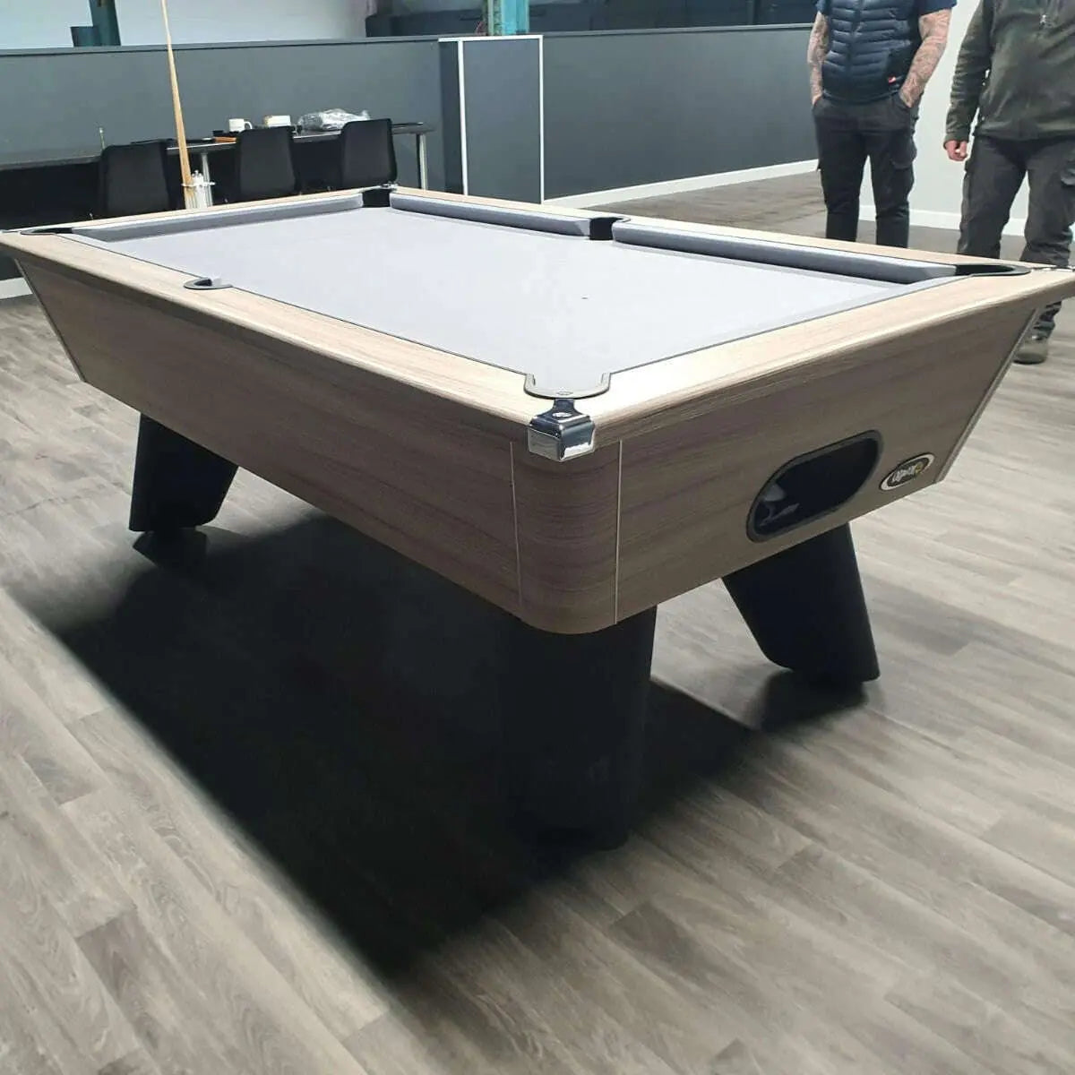 Pool table in an indoor setting with two people in the background