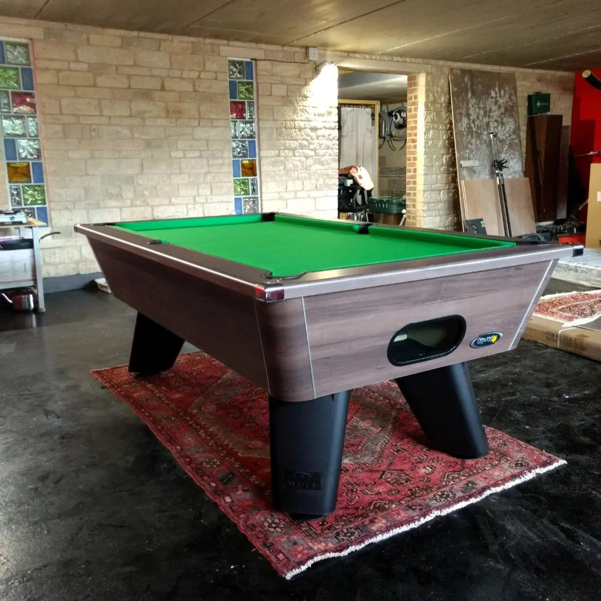 Pool table with green felt surface in a room with brick walls and a rug.