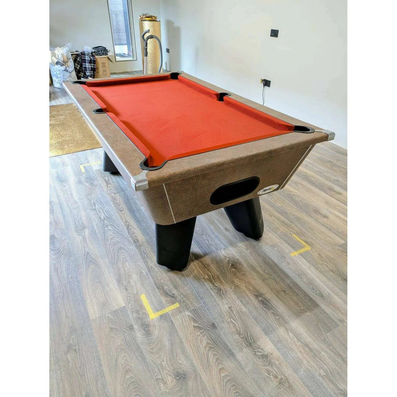 Pool table with red felt surface in a room with wooden flooring.