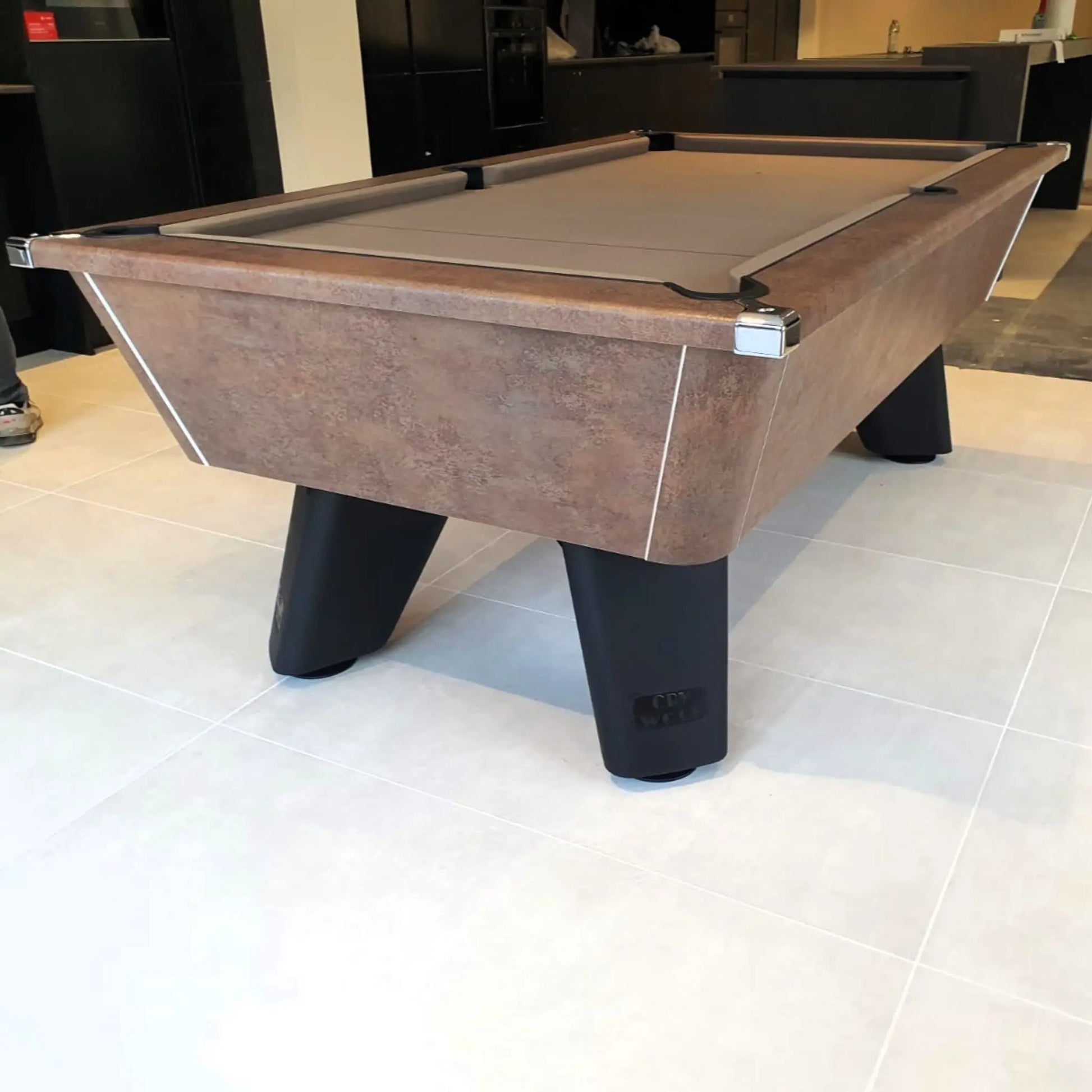 Pool table with wooden finish and black legs on a tiled floor.