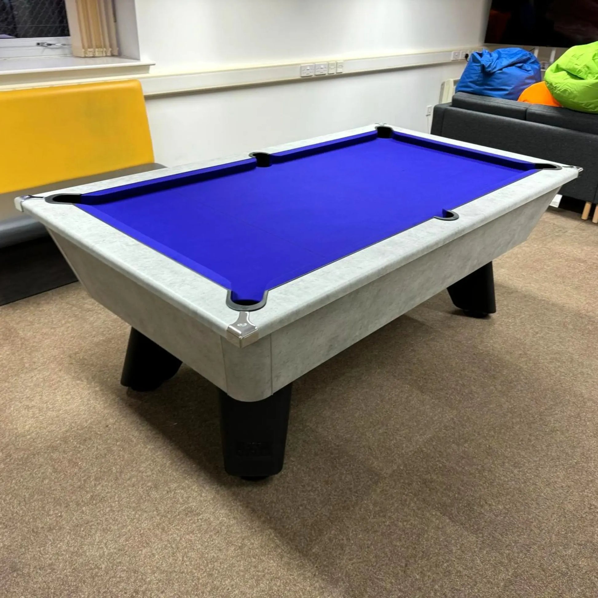Pool table with blue felt in a room with a yellow wall and gray couch.