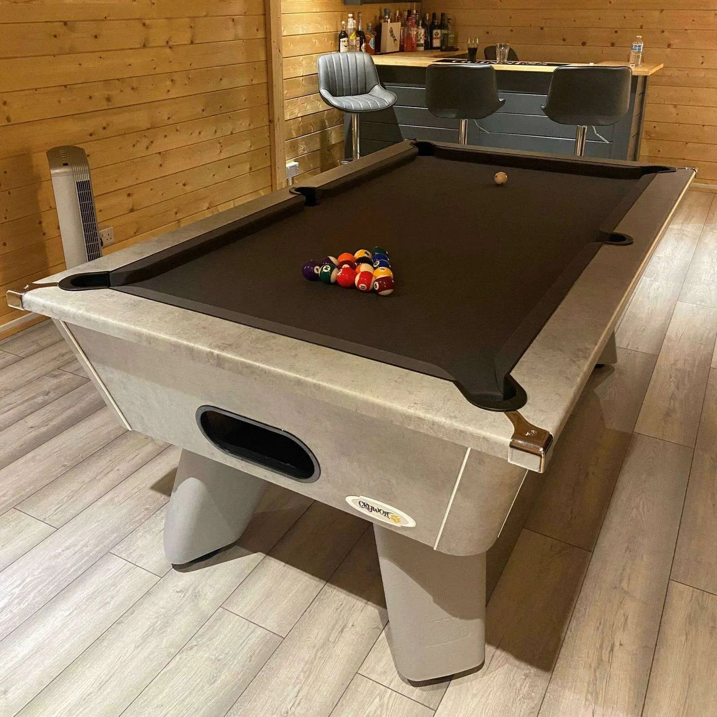 Pool table with billiard balls in a room with wooden walls and a bar.