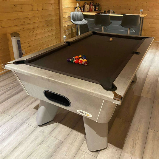 Pool table with billiard balls in a room with wooden walls and a bar.