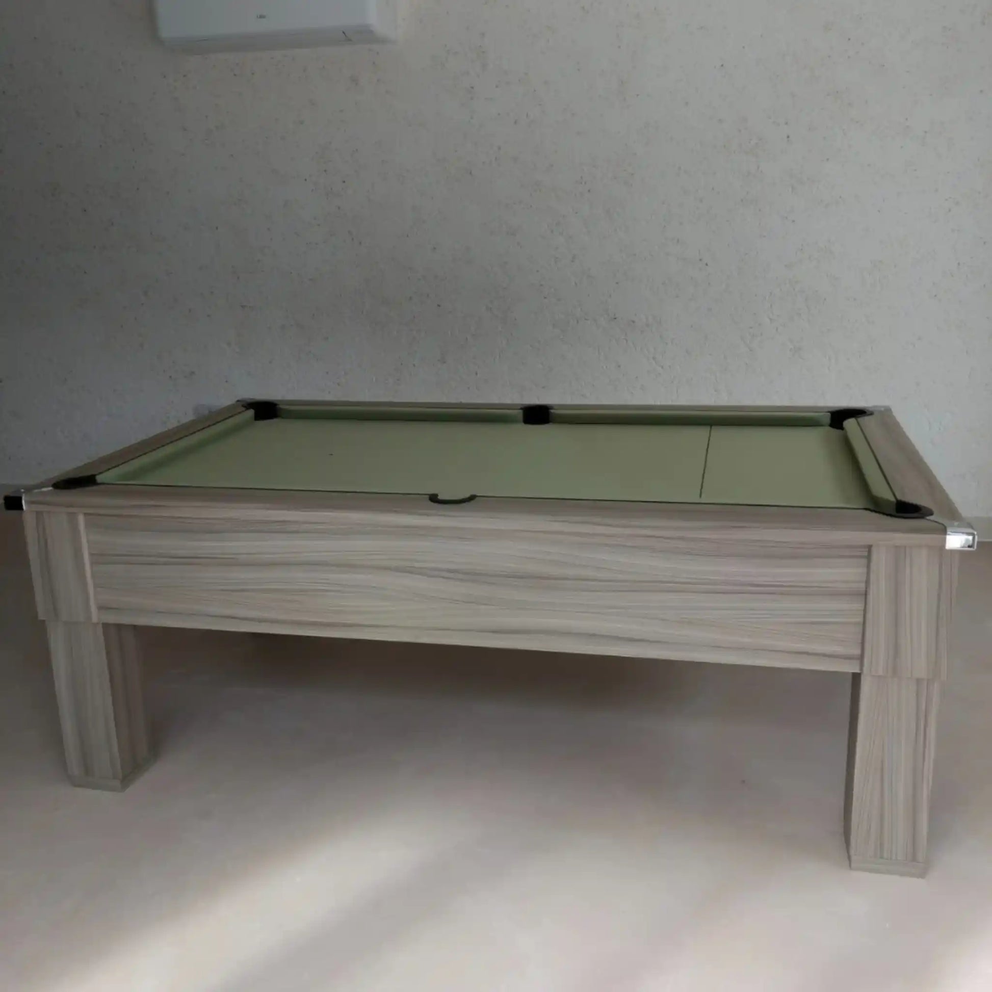 Pool table with green felt surface and wooden frame against a plain wall.