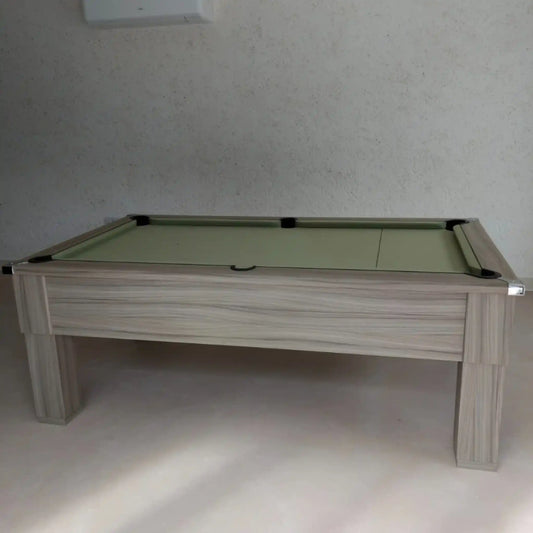 Pool table with green felt surface and wooden frame against a plain wall.