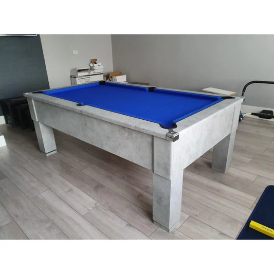 A rectangular pool table with a bright blue felt playing surface and a light grey concrete-look frame, shown in an indoor room with wood-look flooring.