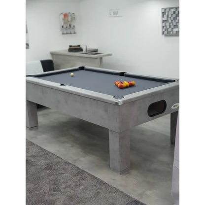 A modern pool table with a gray concrete-look frame and dark gray felt surface, shown in a minimalist indoor room with white walls and a gray rug.