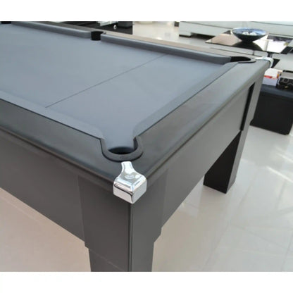 A close-up of a dark gray pool table corner with a white metal ball stopper and a black pocket, set in a bright modern room with light-colored tiled floors.