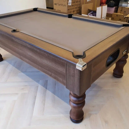 A wooden pool table with a grey felt playing surface, with cardboard boxes in the background.