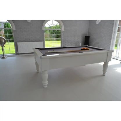 A white wooden pool table with a dark felt surface and colorful ball rack, set in a bright, modern room with white brick walls and large arched windows.