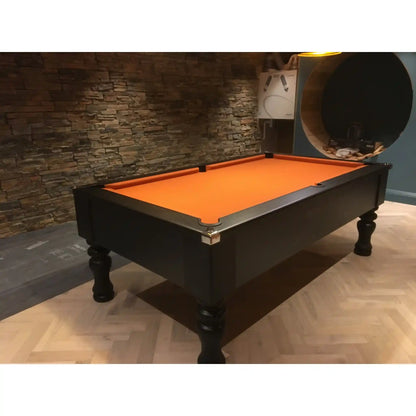 A black pool table with a bright orange felt playing surface, positioned in a modern room with a blue accent wall, a circular window-like feature, and warm brown walls under pendant lights.
