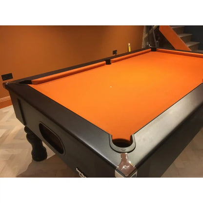 A pool table with a bright orange felt surface and a dark gray or black wooden frame, photographed in an indoor room with an orange-brown wall and light wood flooring.