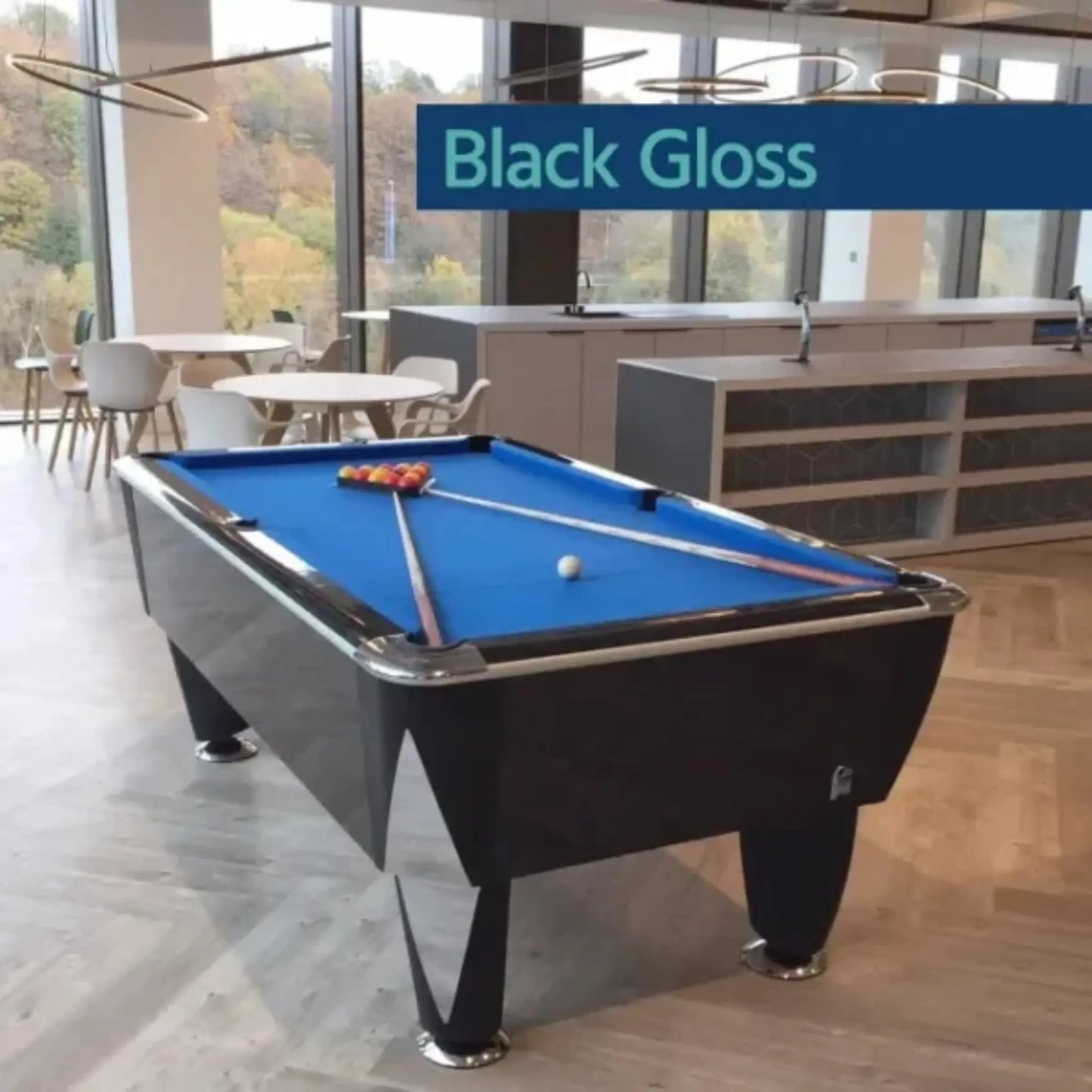 Pool table with blue felt and black frame in a modern room with large windows.